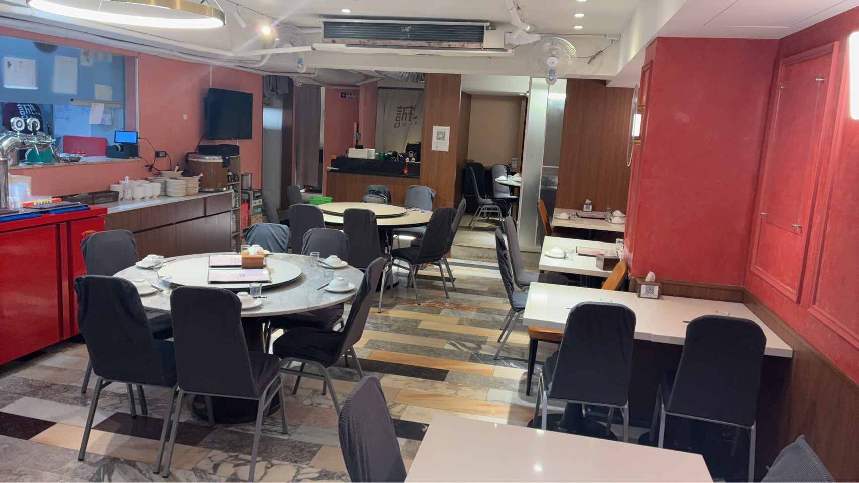 空無一人的餐廳內部，紅色牆面，擺有圓桌、方桌與深灰色座椅